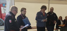 Vier Malteser-Mitarbeitende stehen in einem Zelt und lesen aus Unterlagen bei einer Veranstaltung vor.
