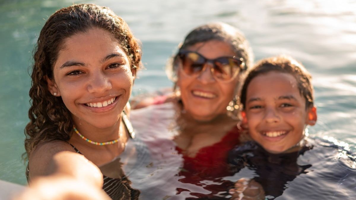 Ältere lächelnde Frau mit Sonnenbrille mit zwei Kindern bis zum Hals im Wasser.