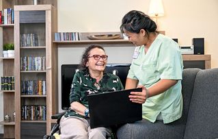 Zwei Frauen sitzen lachend auf dem Sofa und schauen gemeinsam auf einen Laptop drauf