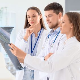 Drei Ärzte betrachten gemeinsam eine Röntgenaufnahme und diskutieren die Diagnose.