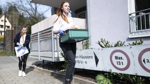 Zwei junge Frauen mit Einmalhandschuhen liefern Einkäufe aus.