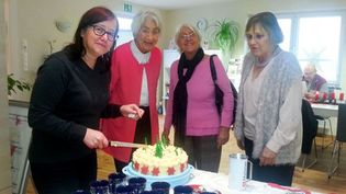 Vier Frauen stehen um eine weihnachtlich dekorierte Torte, eine schneidet sie gerade mit einem Messer an.