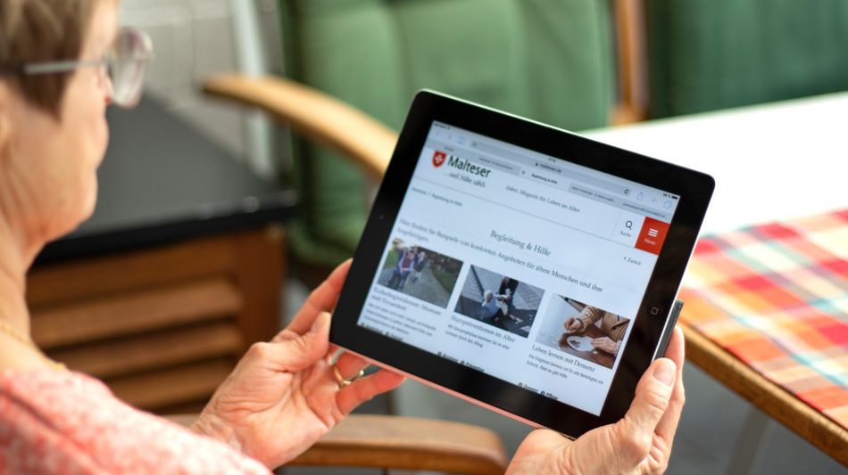 Älter Frau hält ein Tablett in den Händen und schaut auf den Bildschirm.