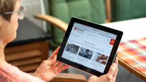 Älter Frau hält ein Tablett in den Händen und schaut auf den Bildschirm.