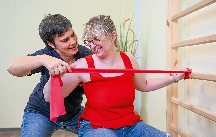 Eine Pflegerin hilft einer jungen Frau bei einer Übung mit einem Terraband