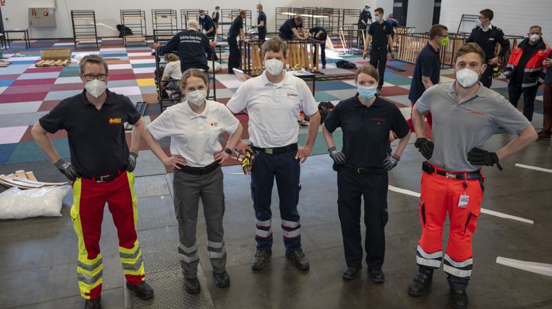 Menschen mit Einsatzkleidung verschiedener Hilfsorganisationen beim Aufbau einer Notunterkunft für Geflüchtete