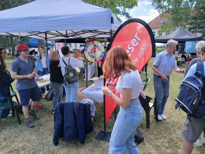 Viele Mensche bewege sich am Stand der Malteser beim Kulturcampus. Im Vordergrund steht ein offenes Zelt mit einer roten Beachflag. Im Zelt und daneben sind viele Besucher und Malteser.