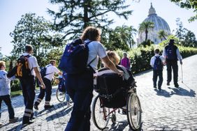 Eine Gruppe von Maltesern und Pilgern, zum Teil im Rollstuhl, laufen auf einem gepflasterten Weg durch den Vatikan.