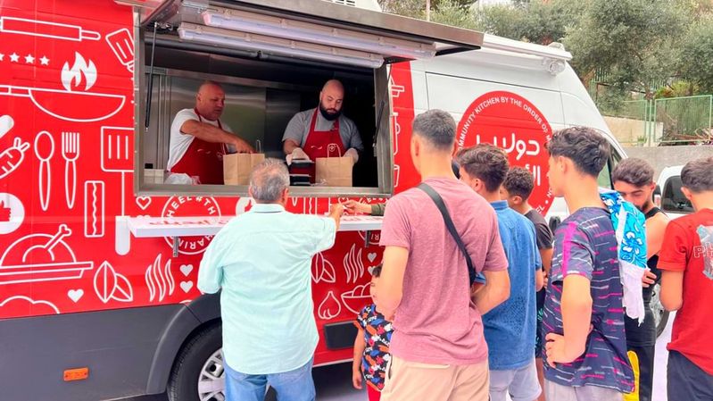 Ein roter Foodtruck, vor dem Menschen auf Essenspakete warten.