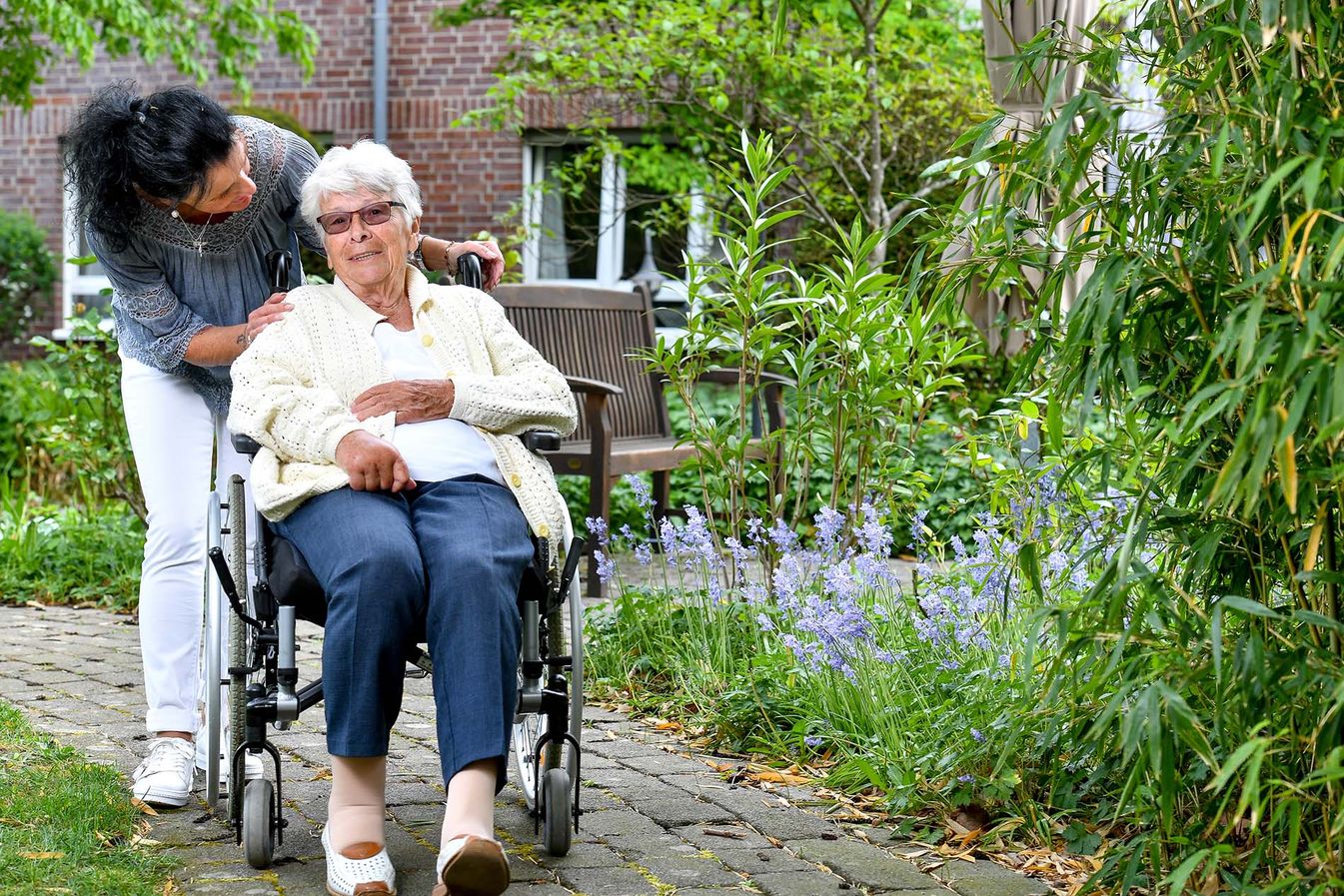 Pflegerin und Bewohnerin gehen spazieren in der Gartenanlage