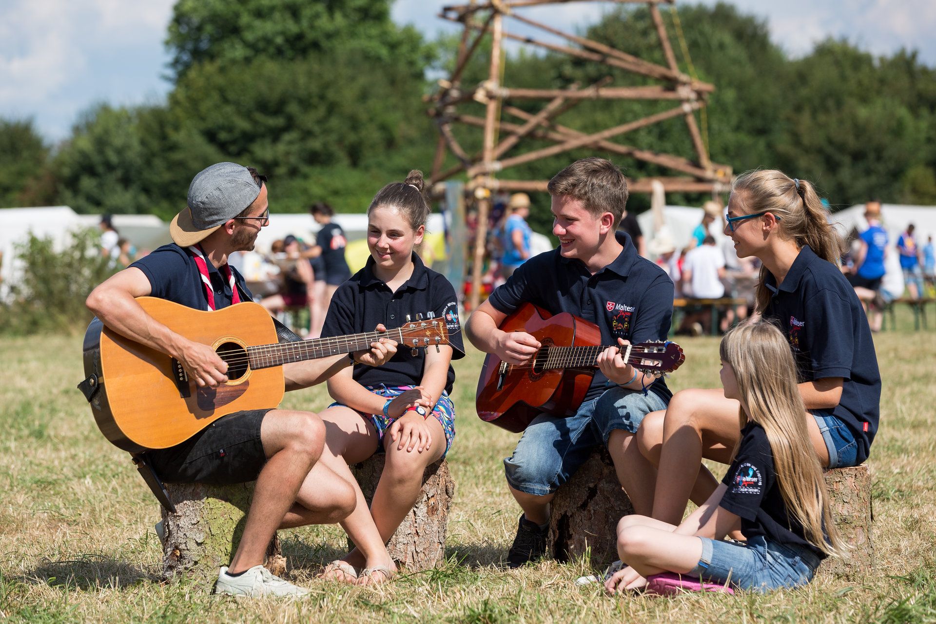 Jugendliche sitzen in einem Halbkreis und spielen gemeinsam Gitarre.