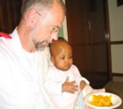 A man holds a young child while she eats.