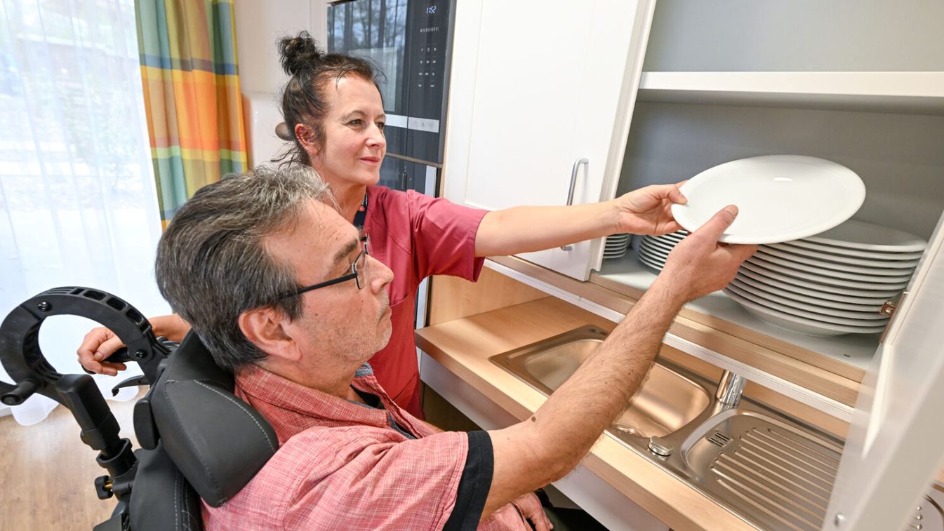Eine Pflegerin und ein Patient im Rollstuhl beim gemeinsamen Teller wegräumen