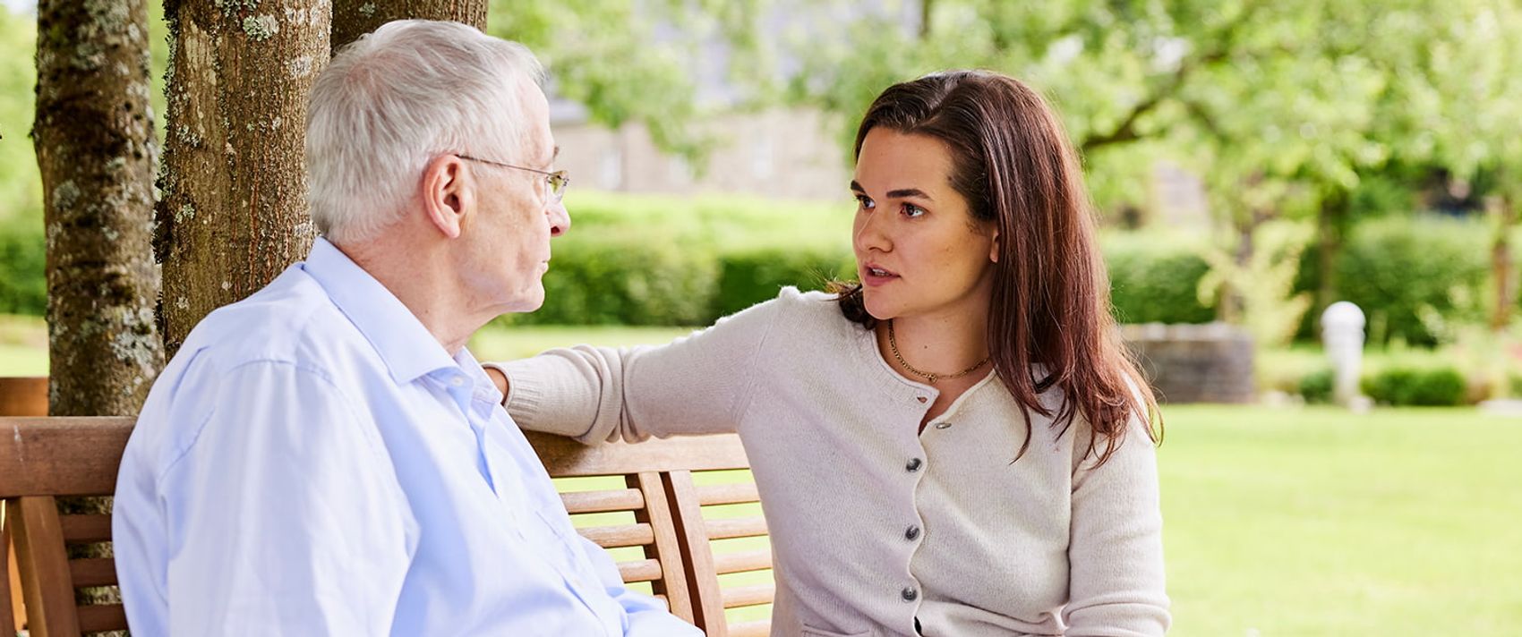 Eine jüngere Frau berät einen älteren Mann zur Patientenverfügung. Sie sitzen im Garten auf einer Bank.