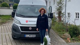 Mitarbeiterin der Malteser steht mit Einkaufstasche vor dem Malteser Einkaufsbus