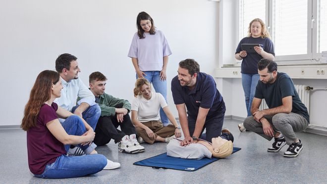 Ein Mann zeigt mehreren Personen die Herzdruckmassage an einer Übungspuppe.