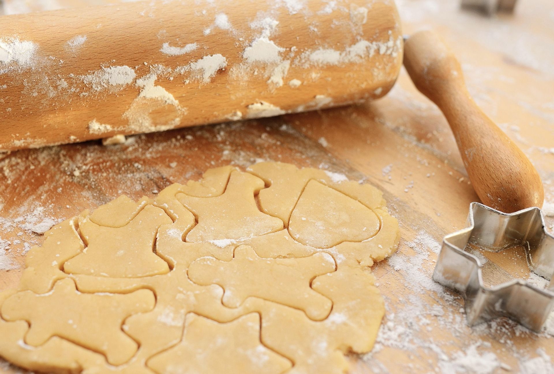 Nudelholz mit Teig, auf dem die Abdrücke von weihnachtlichen Ausstechern zu sehen sind, Mehl, Stern-Ausstecher