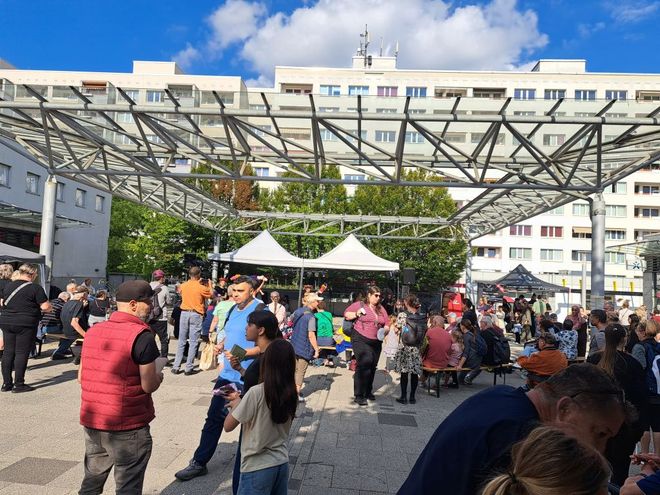 Viele Menschen genießen das Bürgerfest unter freiem Himmel. Im Hintergrund ist ein Wohnblock von Prohlis zu sehen. Die Sonne scheint.
