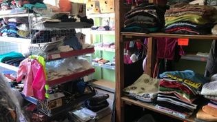 Malteser Regalraum mit mehreren Metall- und Holzregalen, auf denen gefaltete Kleidung und Taschen liegen.Annaberg-Buchholz Dienstleistung Kleiderkammer