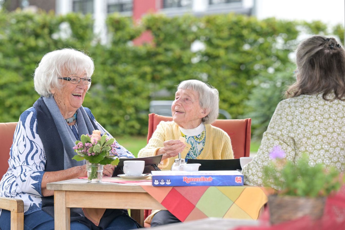 Drei ältere Frauen sitzen draußen gemeinsam am Tisch und unterhalten sich