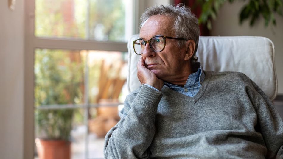 Älterer Mann mit gelangweiltem Gesichtsausdruck schaut aus einem Fenster.