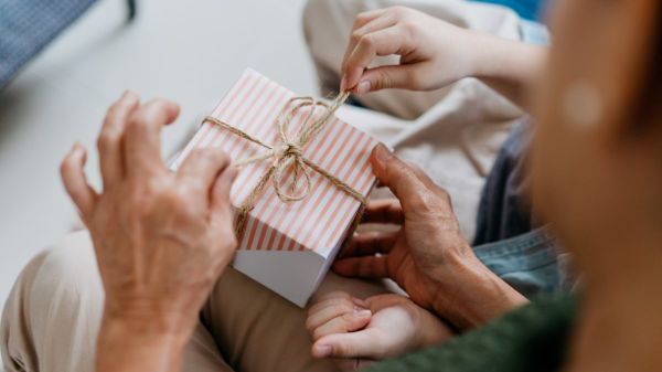 Zwei Paar Hände, die ein Geschenk auspacken.