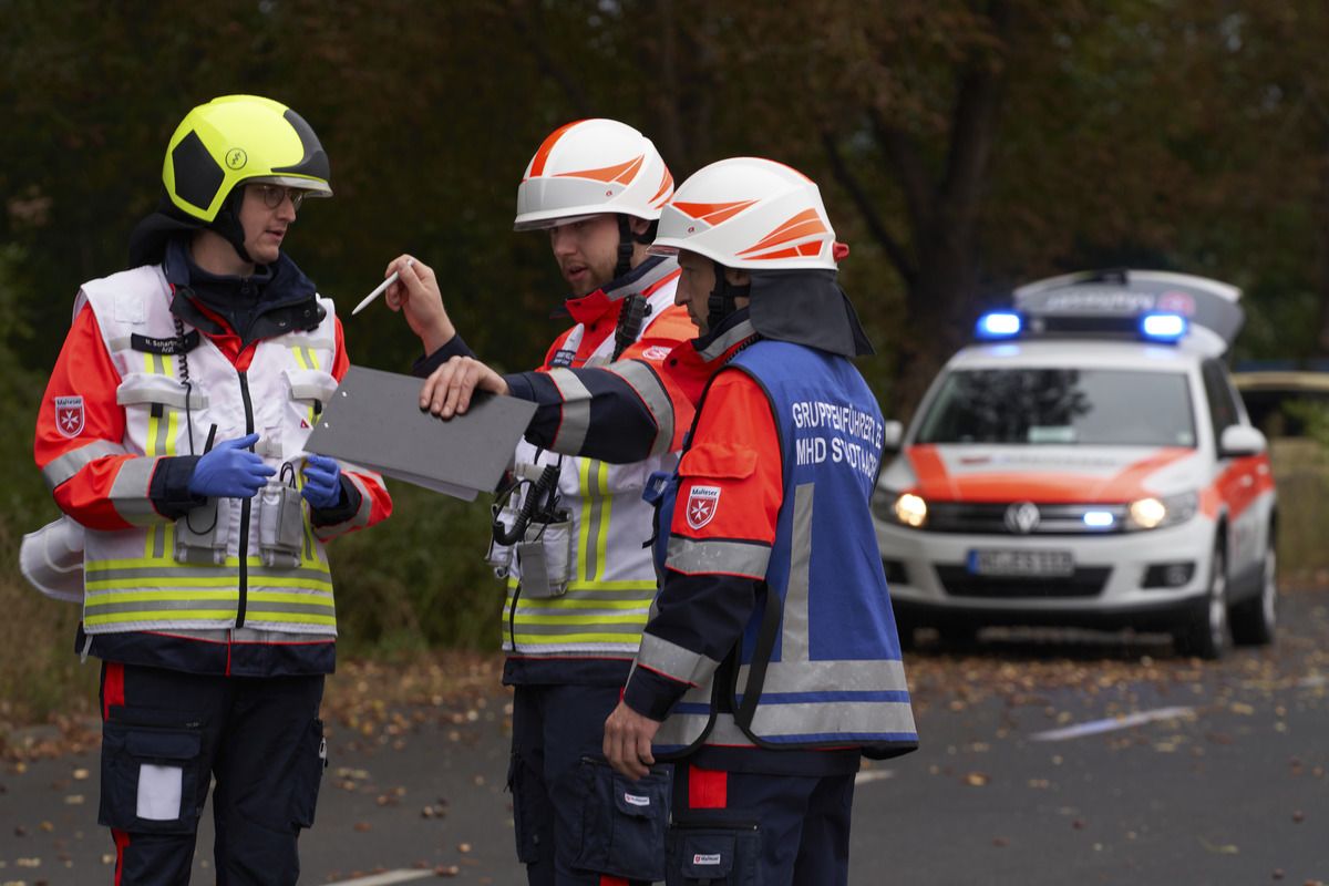Drei Einsatzkräfte mit Funktions-Kennzeichnungswesten stehen auf der Straße und sprechen miteinander. 