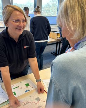 Eine Frau in Malteser Dienstkleidung erklärt die Straßenkarte, die auf dem Tisch liegt.
