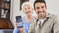 Mutter und Sohn sitzen glücklich auf einem Sofa, der Sohn hält sein Handy mit der HNR+-App in die Kamera