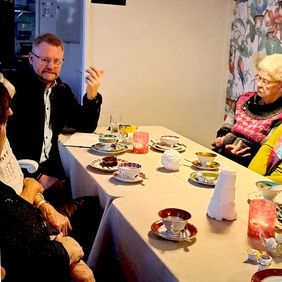 Ein Mann sitzt an einem Tisch. Er spricht zu einigen Frauen.