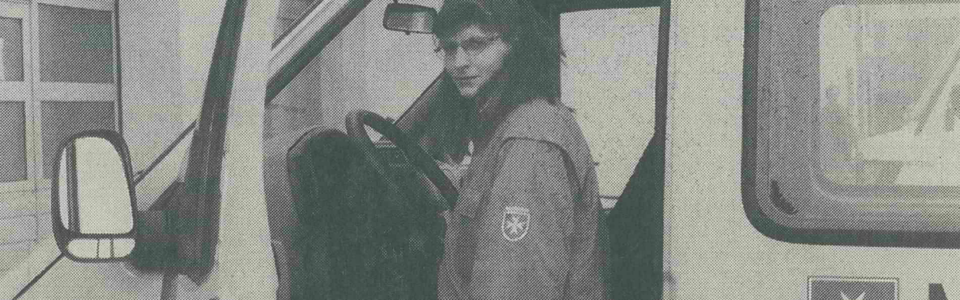 Ein monochromes Zeitungsbild einer jungen Frau mit Brille, die in ein Fahrzeug der Malteser in Deutschland steigt.