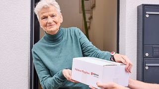 Eine ältere Frau mit kurzen grauen Haaren nimmt an der Haustür ein Päckchen mit der Malteser Pflegebox entgegen.