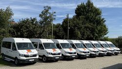 Acht Behindertentransportwagen der Malteser Erding stehen aufgereiht auf einem Parkplatz.