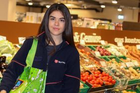 Portrait einer ehrenamtlichen Einkaufshelferin der Malteser in der Gemüseabteilung eines Supermarktes.
