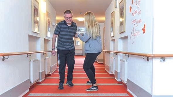 Eine Pflegerin unterstützt einen Patienten beim Lauftraining im Flur
