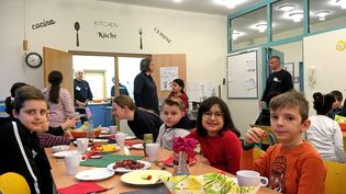 Buben und Mädchen sitzen an einem bunt gedeckten Frühstückstisch in einer Schulkantine