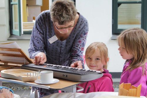 Eine Frau, mit zwei kleinen Mädchen an ihrer Seite, spielt auf einem E-Piano