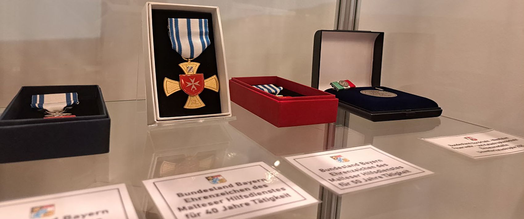 Mehrere silberne und goldene Malteser-Medaillen in einer Vitrine.