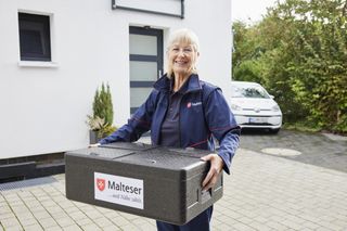 Mitarbeiterin des Malteser Menüservice trägt Essensbox.