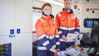 Zwei Mitarbeitende des Malteser Rettungsdienstes lächeln in die Kamera.