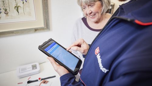 Eine Seniorin schaut auf das Tablet des Hausnotruf Bereitschaftsdienst Mitarbeiters.