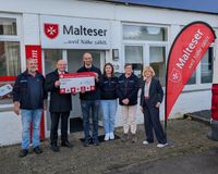 Ein Vertreter der Sparkasse LeerWittmund überreicht ehrenamtlichen Helferinnen und Helfern vor der Dienststelle Leer einen symbolischen Scheck.