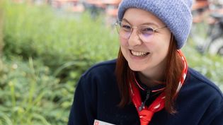 Junge Frau in Malteser Kleidung mit einer grauen Mütze sitzt im Freien an einer Schreibmaschine