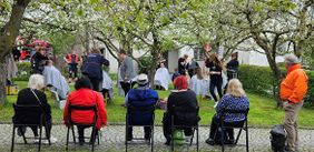 Viele Menschen sitzen in einem Garten, einigen werden die Haare geschnitten.