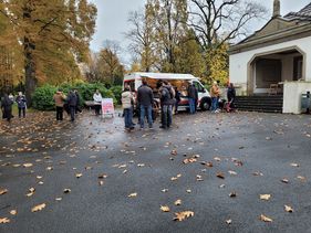 Der Wärmebus vor der Friedhofskapelle auf einem Gladbecker Friedhof, davor sind Grüppchen von Menschen versammelt