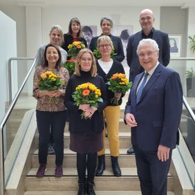Gruppenfoto auf einer Treppe mehrere Personen halten Blumensträuße ein Mann steht vorn im Anzug.