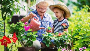 Eine ältere Dame gießt Blumen mit einem jungen Mädchen in einem bunten Garten.