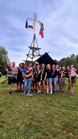 Gruppenfoto von zwanzig Jugendlichen und Gruppenleitungen der Malteser Jugend, die auf einer Wiese vor einem Bannermast stehen. Auf dem Banner steht Bunte Bande.