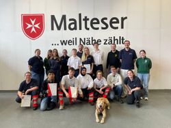 Auf dem Foto sind die Teilnehmenden des diesjährigen Einsatzsanitäterkurses zu sehen, vor dem Hintergrund des Malteser Logo