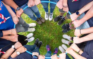 Junge Menschen stehen im Kreis und halten an einem Ring sich gemeinsam fest